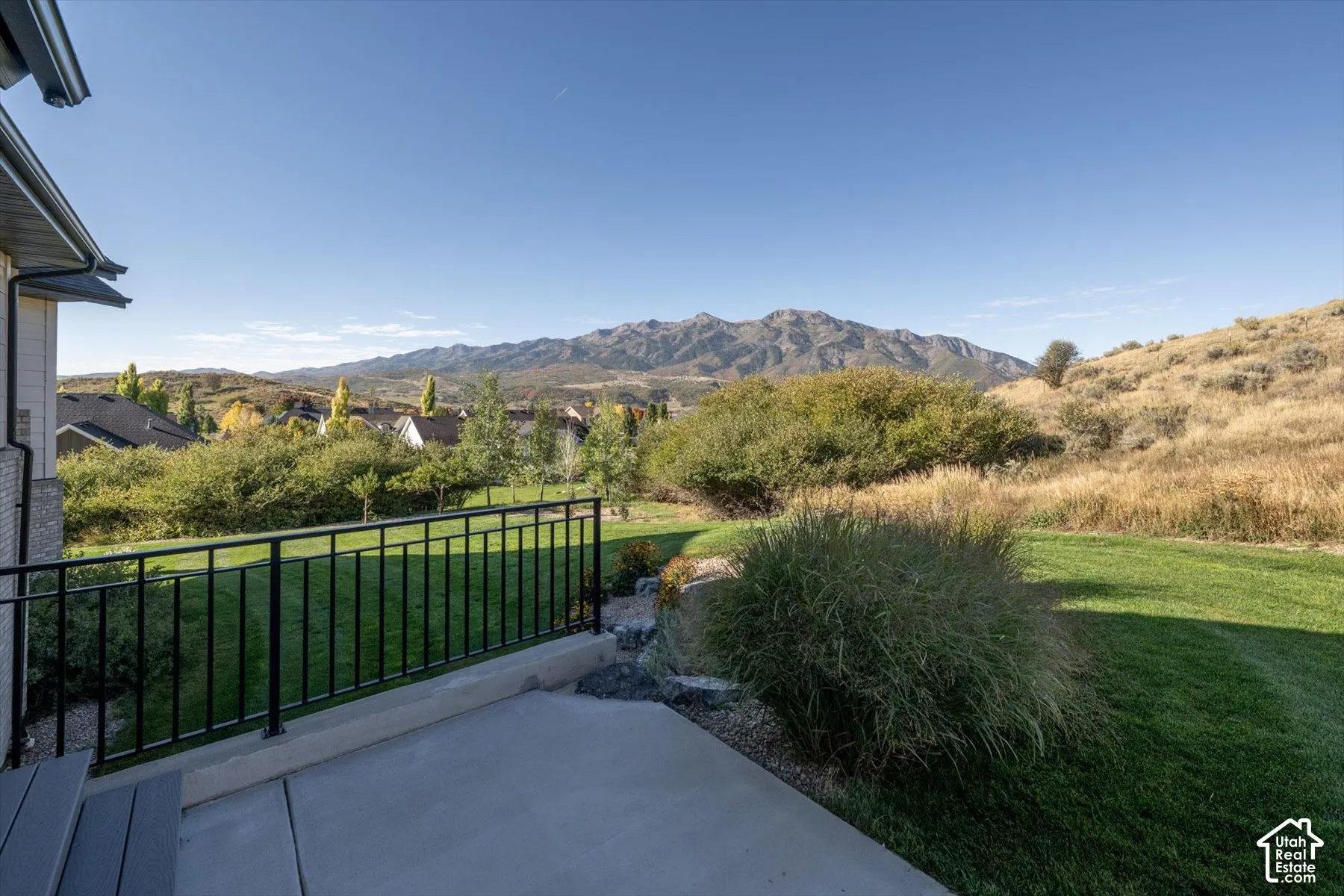Concrete patio with black metal railing, overlooking a green lawn and distant mountains