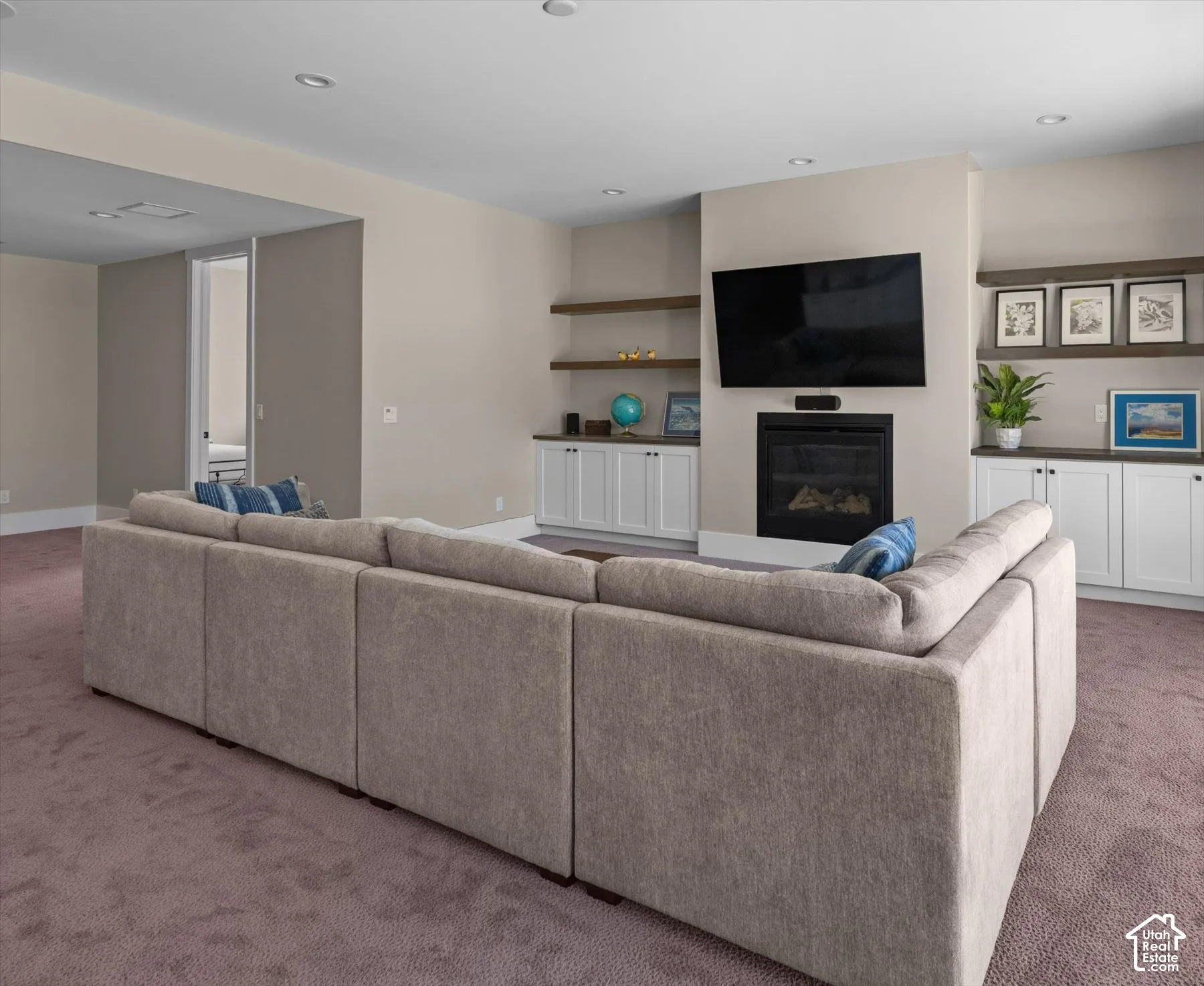 Recessed lighting, built-in cabinetry with floating shelves, and a fireplace with a mounted television