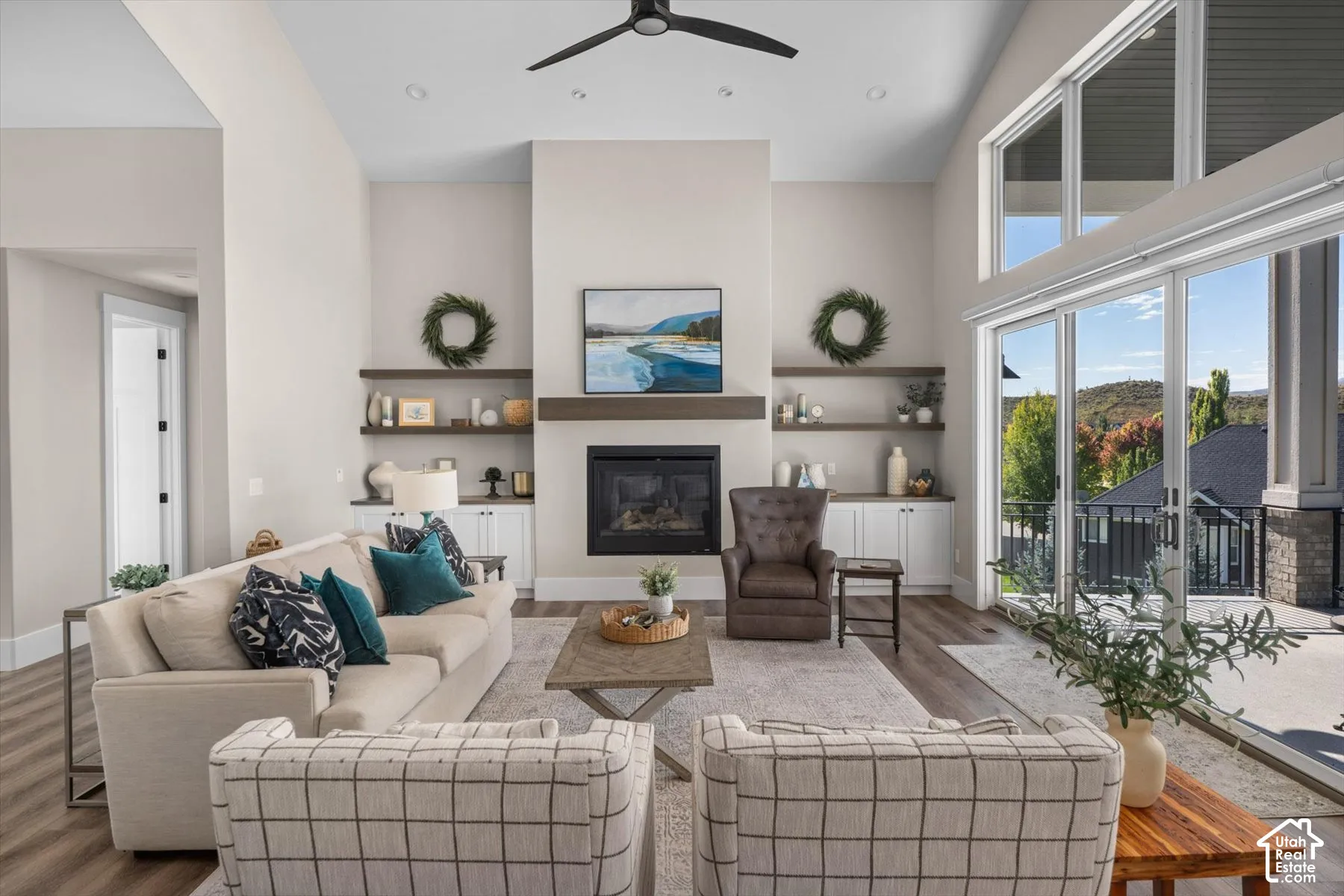 Vaulted ceiling with a ceiling fan, fireplace with a wood-finish mantel, built-in shelving, glass sliding doors, and wood-finish flooring