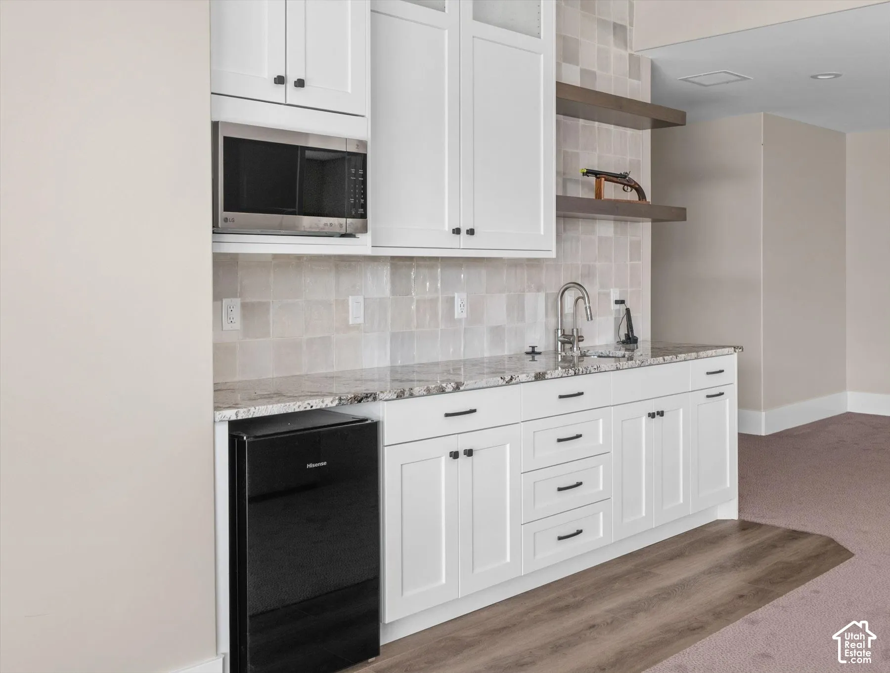 White shaker cabinetry with black hardware, stone countertop, square tile backsplash, stainless steel microwave, and wood-finish flooring
