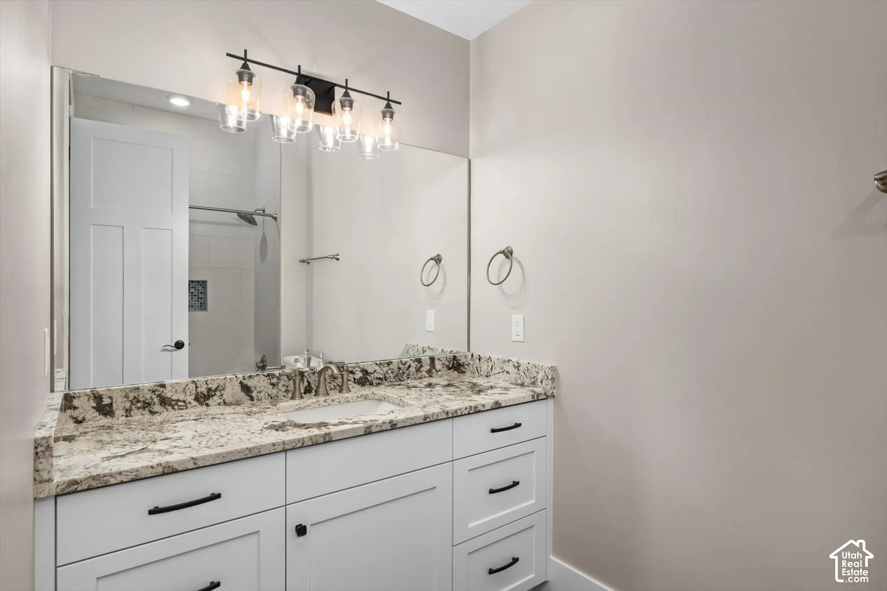 White vanity with black hardware, stone countertop, undermount sink, and full-width mirror