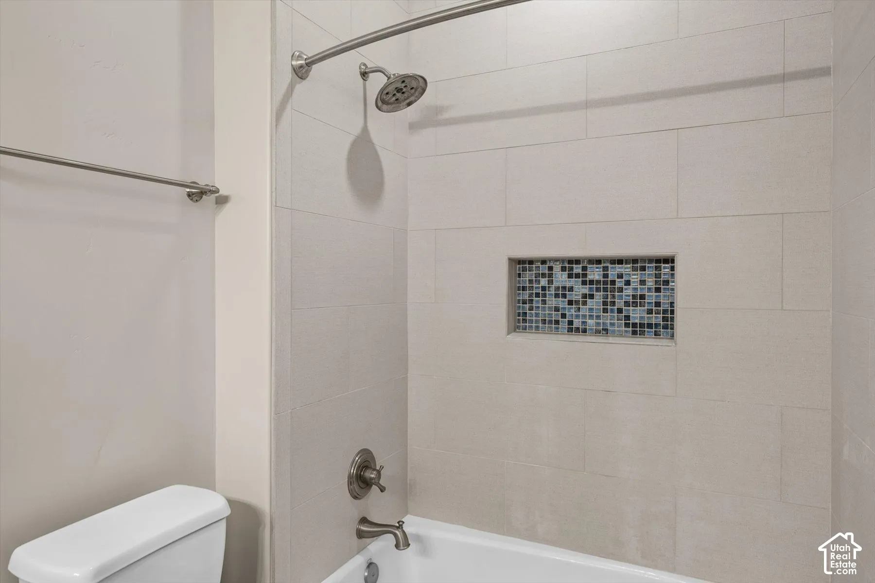 Bathtub with light-toned rectangular tile surround, recessed mosaic tile niche, brushed nickel showerhead, and matching faucet fixtures