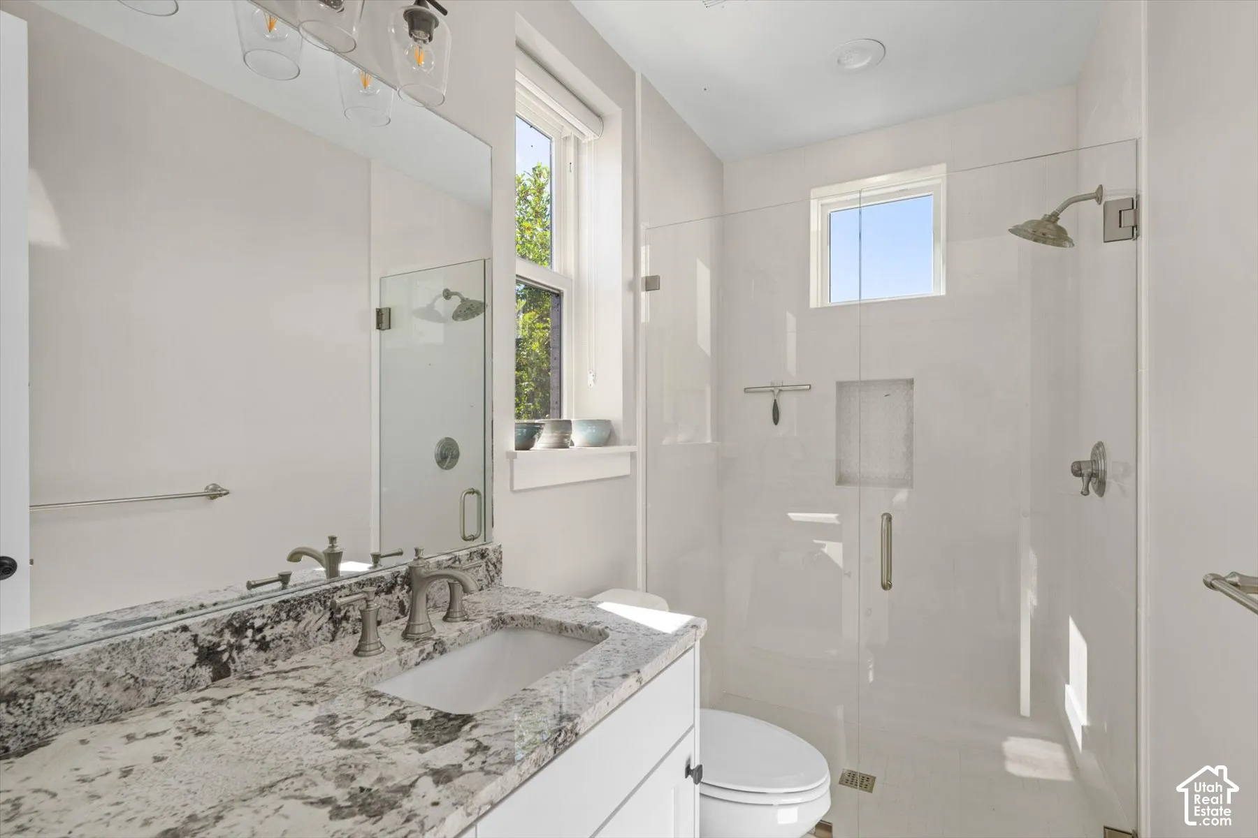 Bathroom featuring a vanity with a stone countertop, a rectangular undermount sink, and a frameless glass shower enclosure with a rain shower head