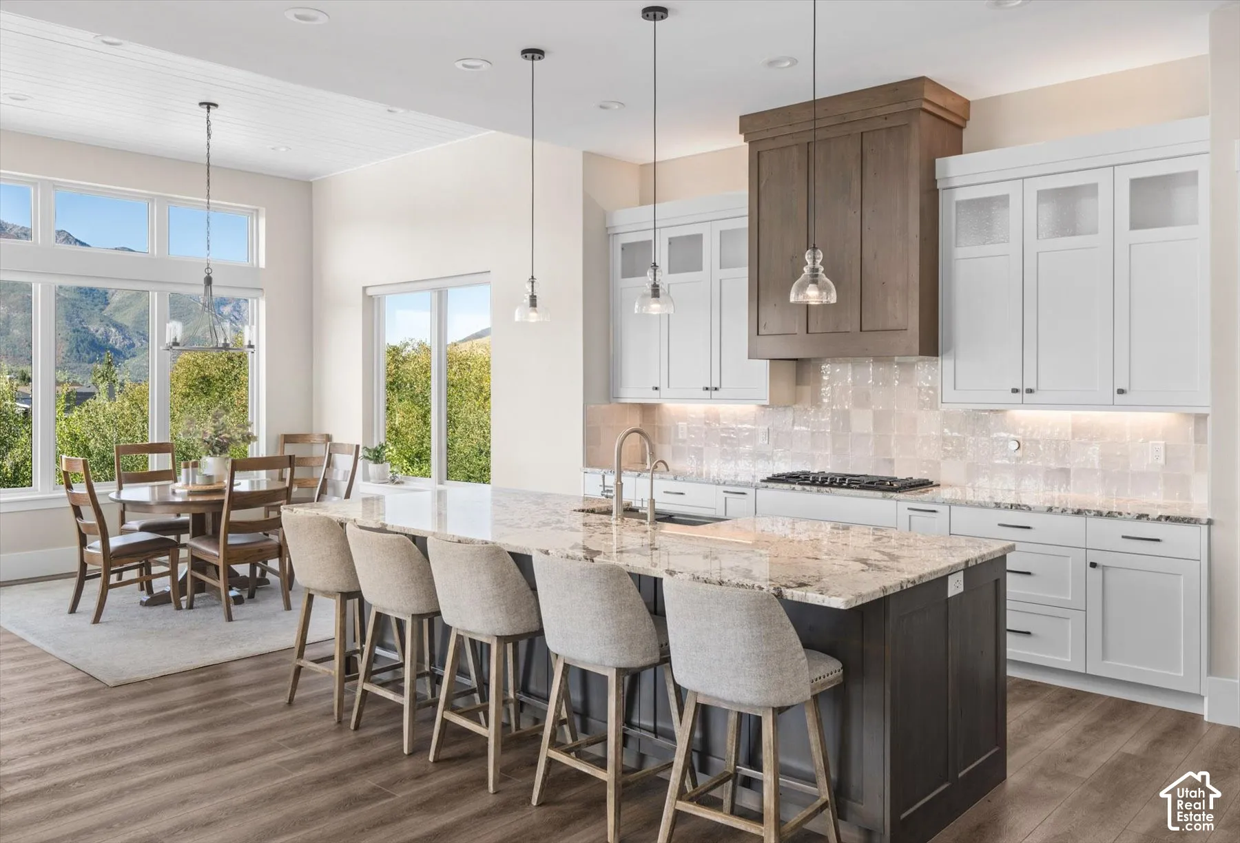 Expansive kitchen with a large island, wood-finish flooring, white cabinetry, integrated range hood, and pendant lighting