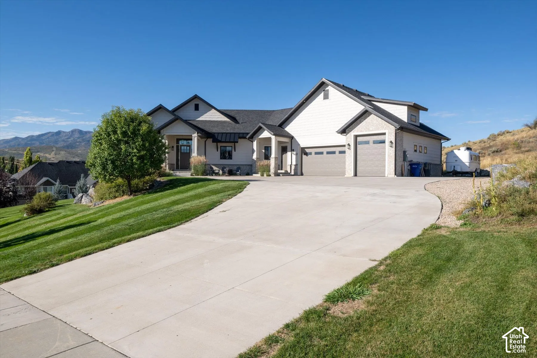 Contemporary residence with two distinct garage doors, a concrete driveway, and a sloped lawn