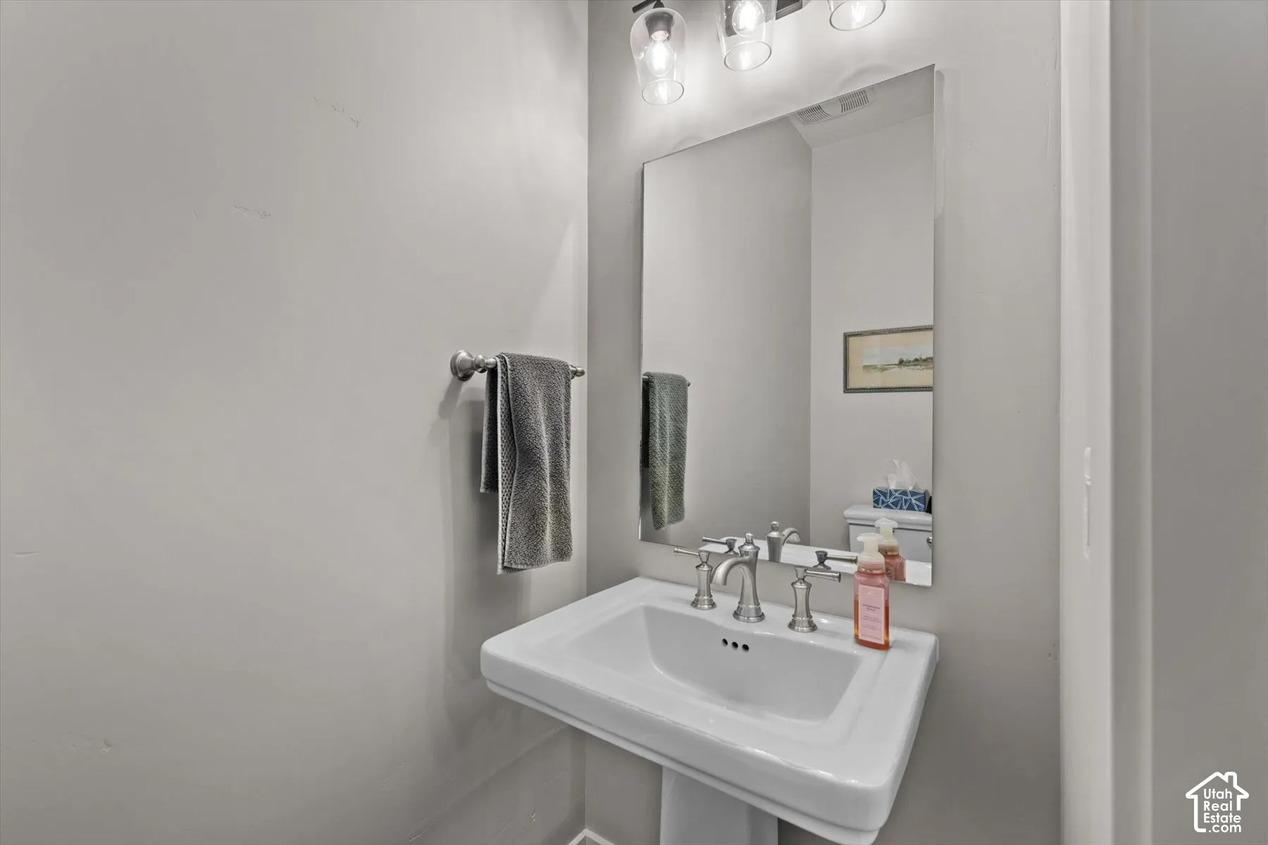 Pedestal sink with brushed nickel faucet, wall-mounted mirror, and overhead vanity lighting