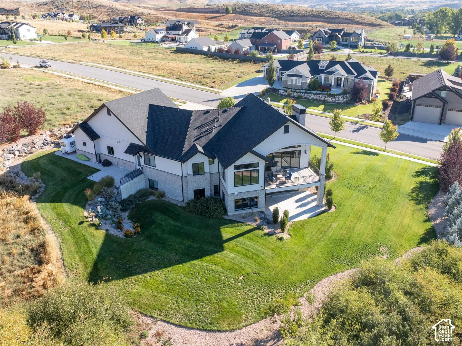 Expansive green lawn surrounding a contemporary-style residence with a covered upper-level deck, lower-level patio, and attached two-car garage