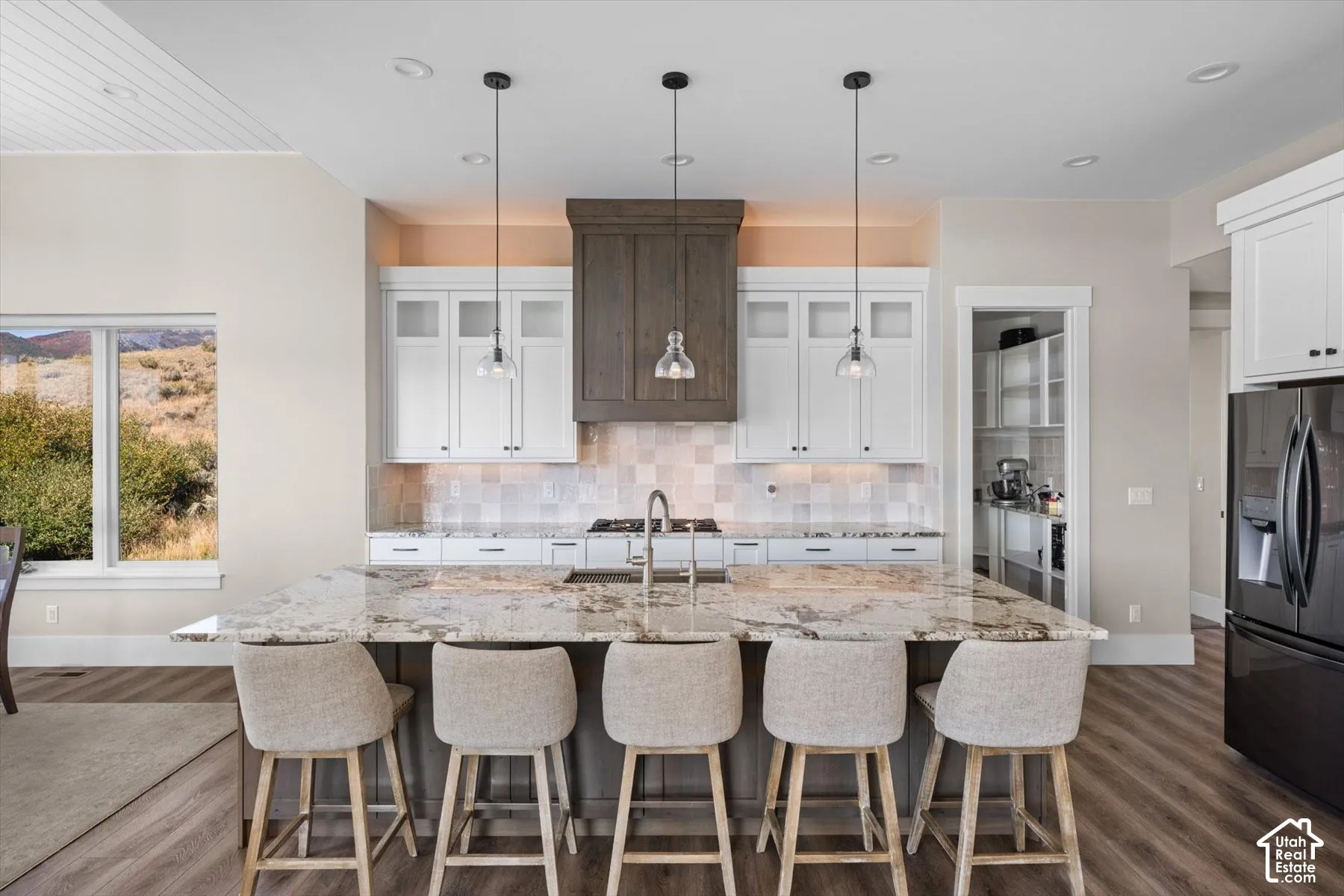 Spacious kitchen island with seating, pendant lighting, white cabinetry, and a full-size refrigerator