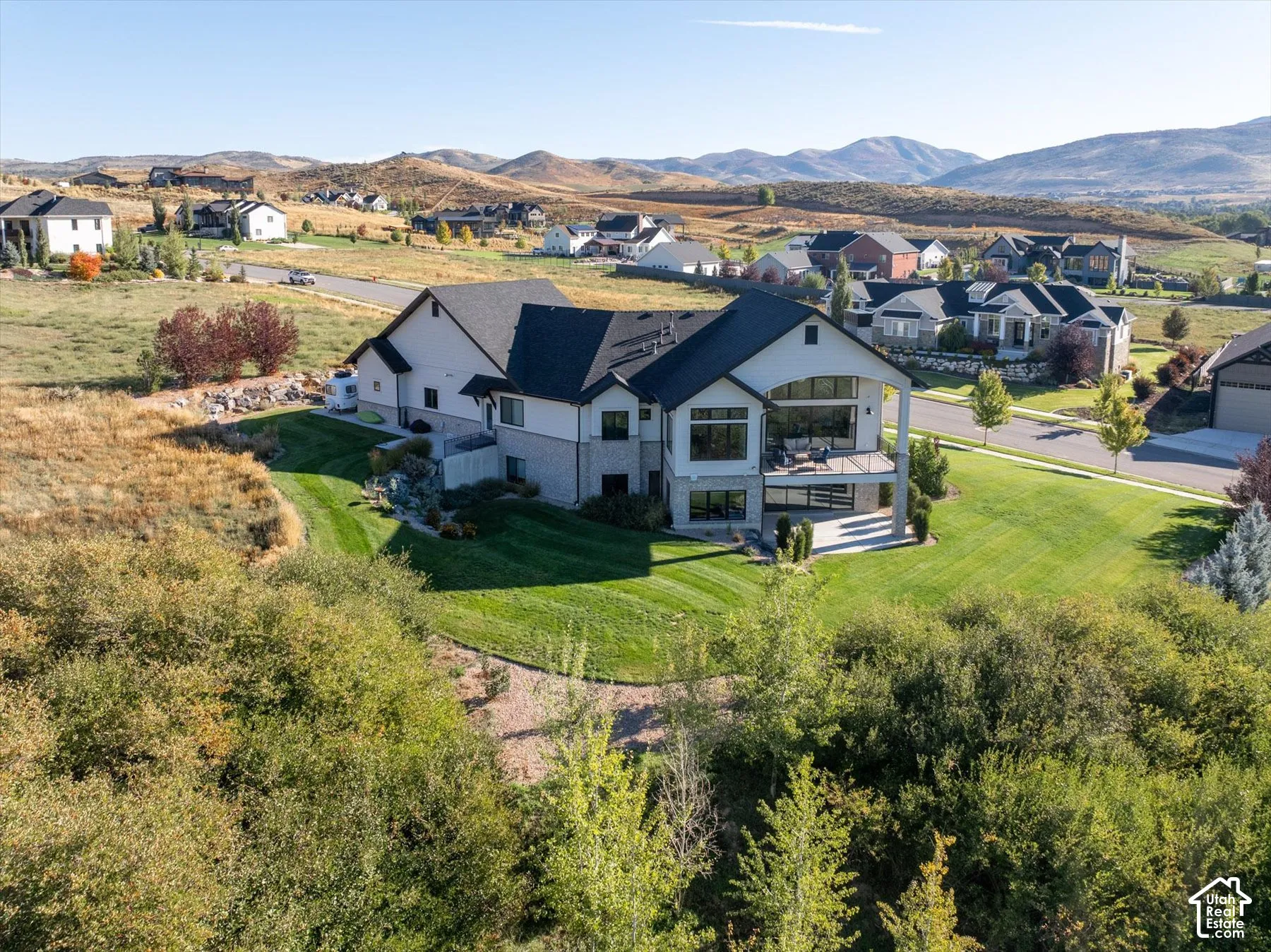 Contemporary exterior design, multi-level structure with multiple balconies, expansive rear lawn, surrounding natural landscape, and distant mountain scenery