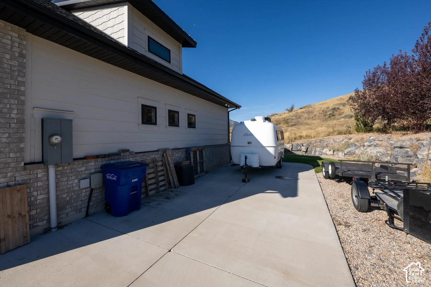 Poured concrete driveway leading to a white siding exterior with a brick foundation