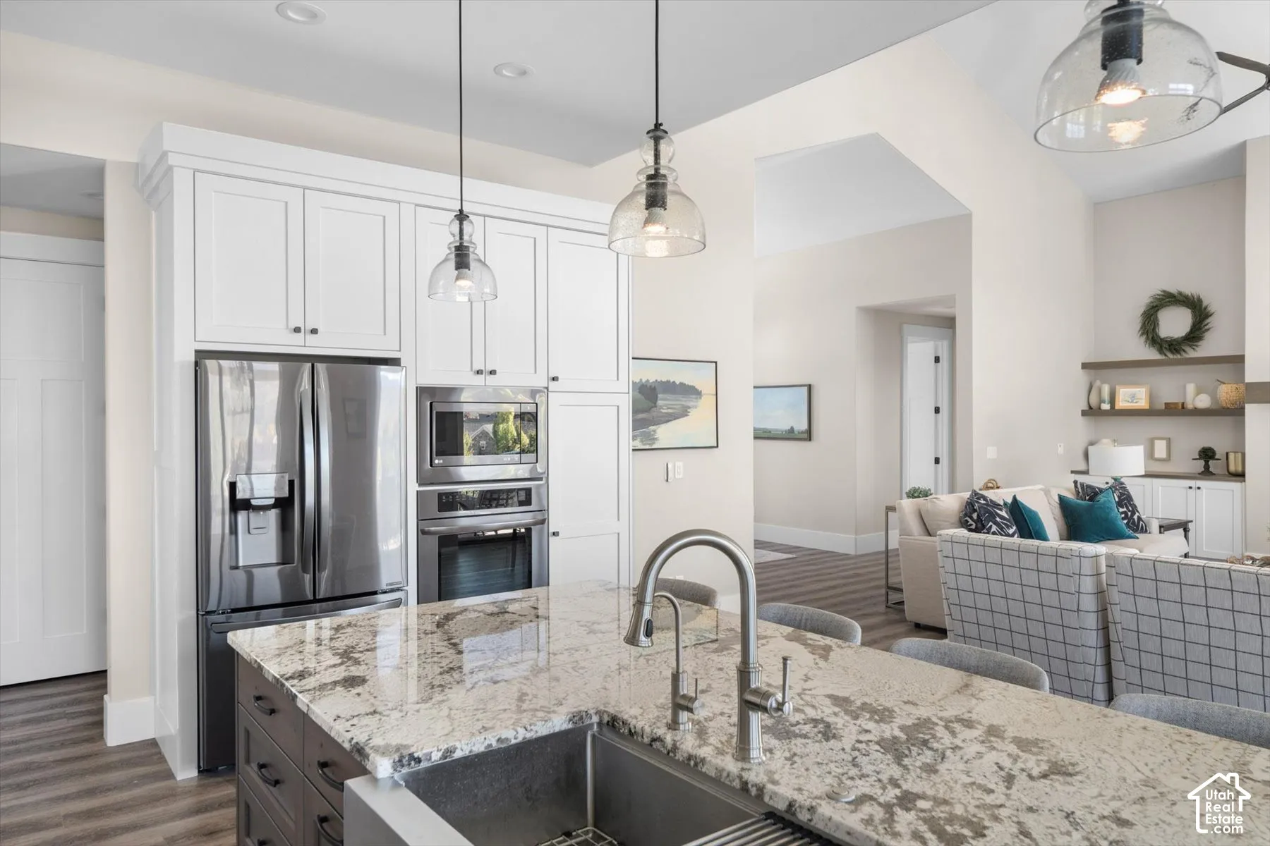Kitchen island with stone countertop and integrated sink, stainless steel appliances, white upper cabinetry, recessed lighting, and wood-finish flooring