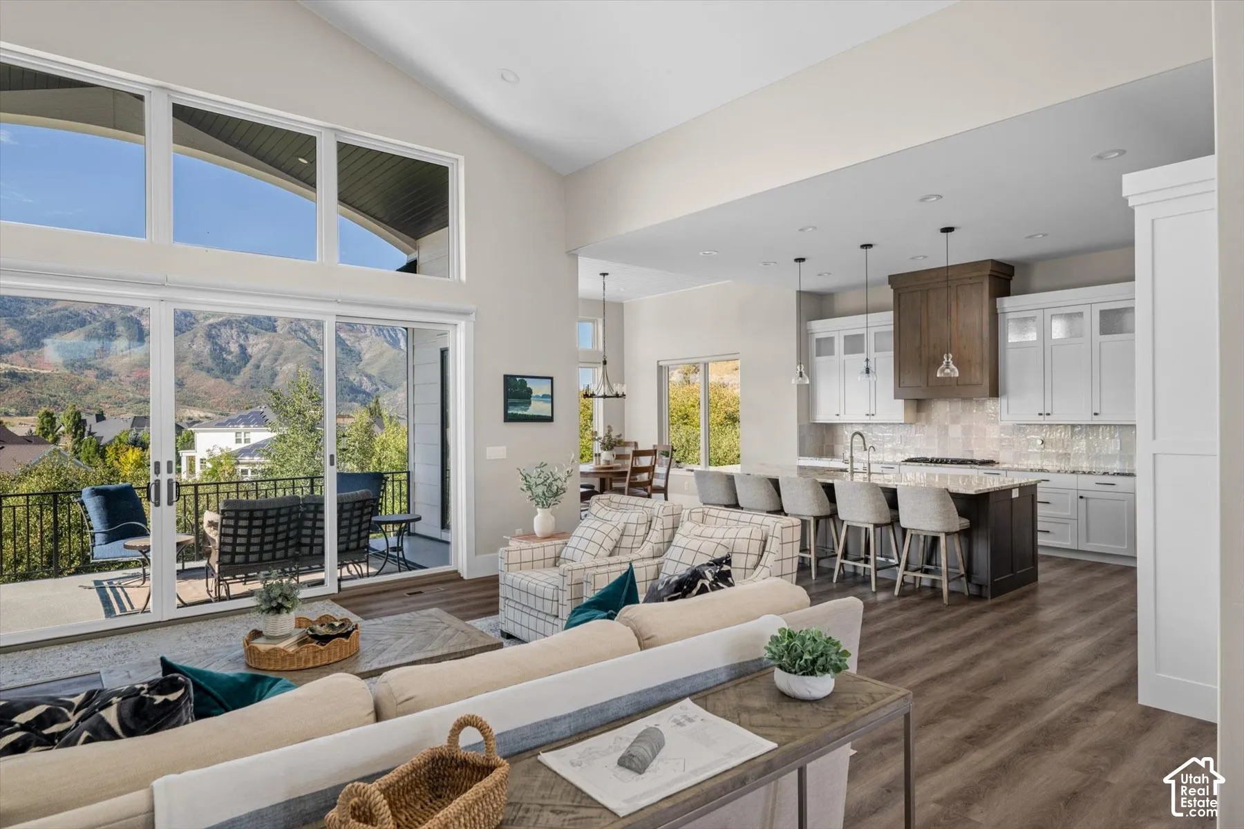 Vaulted ceilings with clerestory windows, expansive sliding glass doors, a large balcony, a central kitchen island with seating, and wood-finish flooring throughout