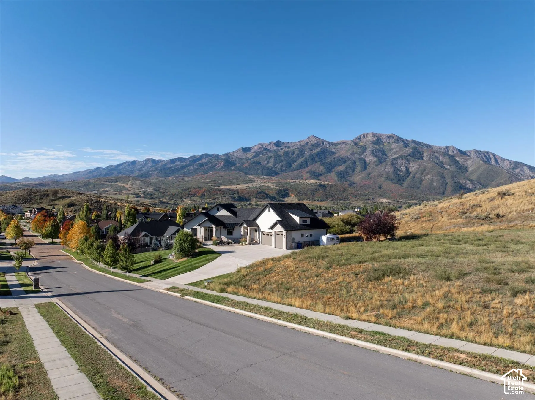 Mountainous terrain backdrop with a residential street, featuring a paved road, concrete sidewalks, and a manicured lawn