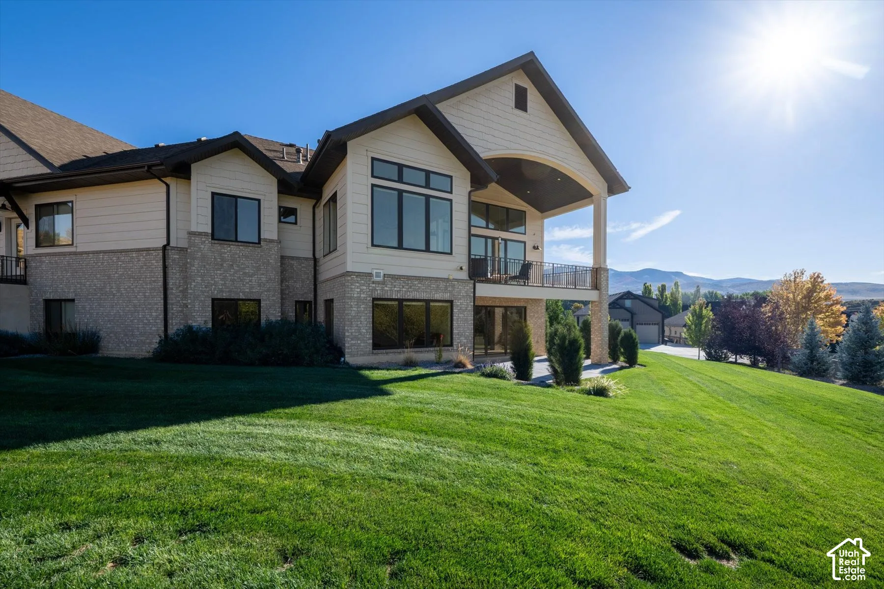 Multi-level residence featuring stone and siding exterior, large windows, an upper-level balcony with metal railing, and a covered patio area