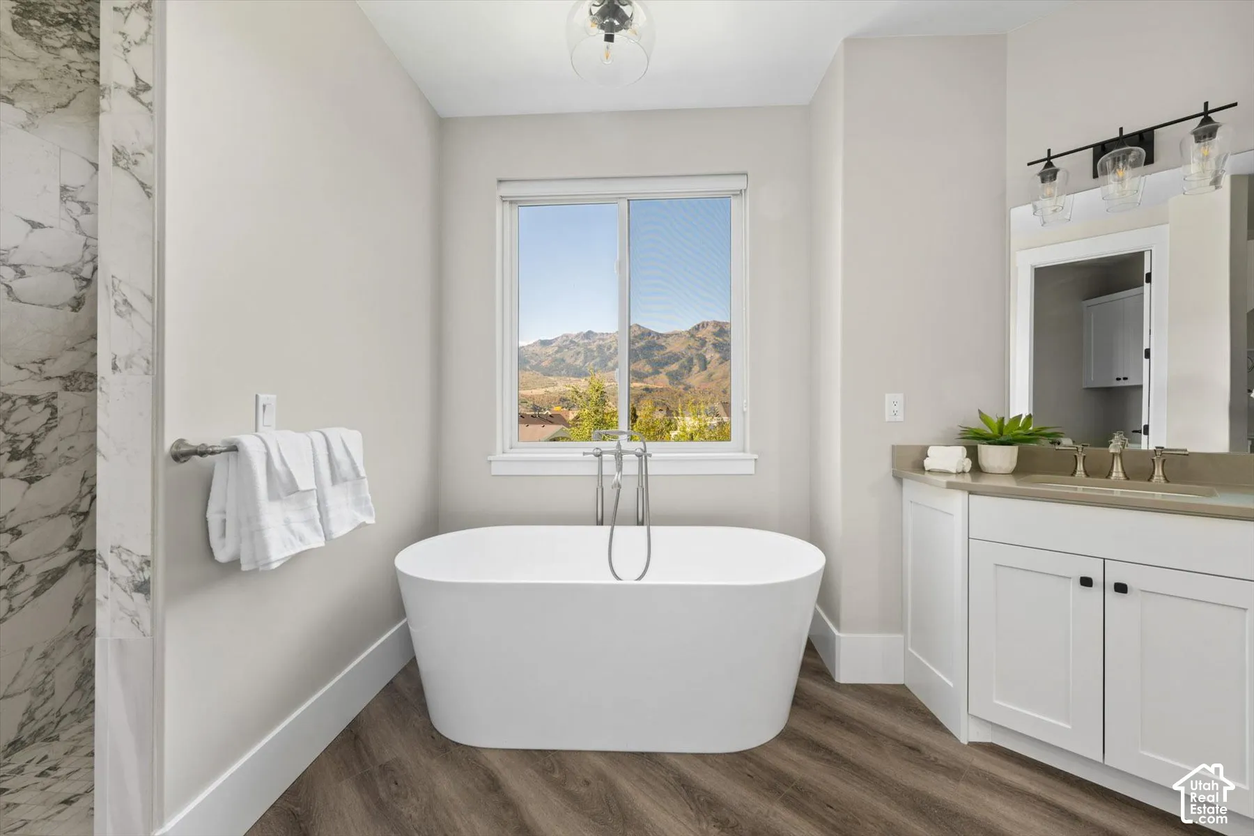 Freestanding soaking tub with a floor-mounted faucet, wood-finish flooring, and a window with mountain scenery