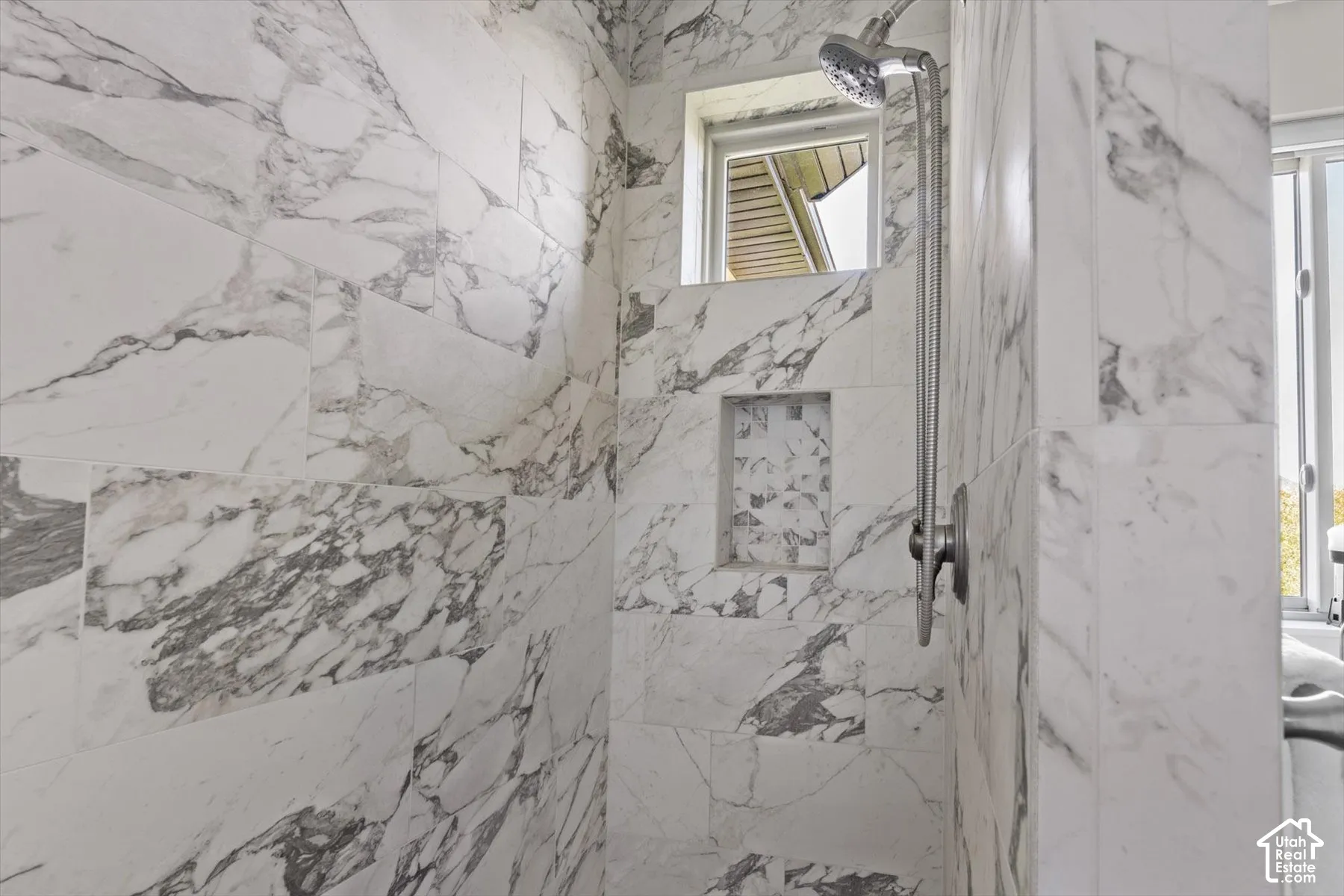 Shower enclosure with large format marble-look tile, built-in shower niche, and a brushed nickel shower head