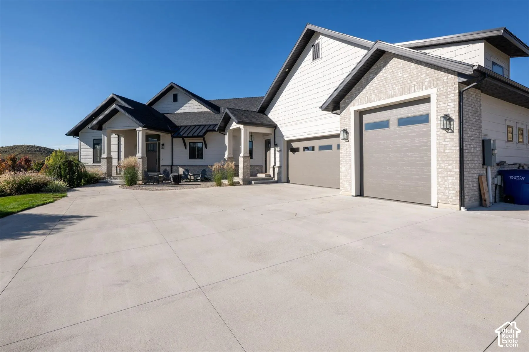 Modern exterior featuring light-colored brick and siding, a multi-car garage with contemporary doors, a concrete driveway, and a covered entry