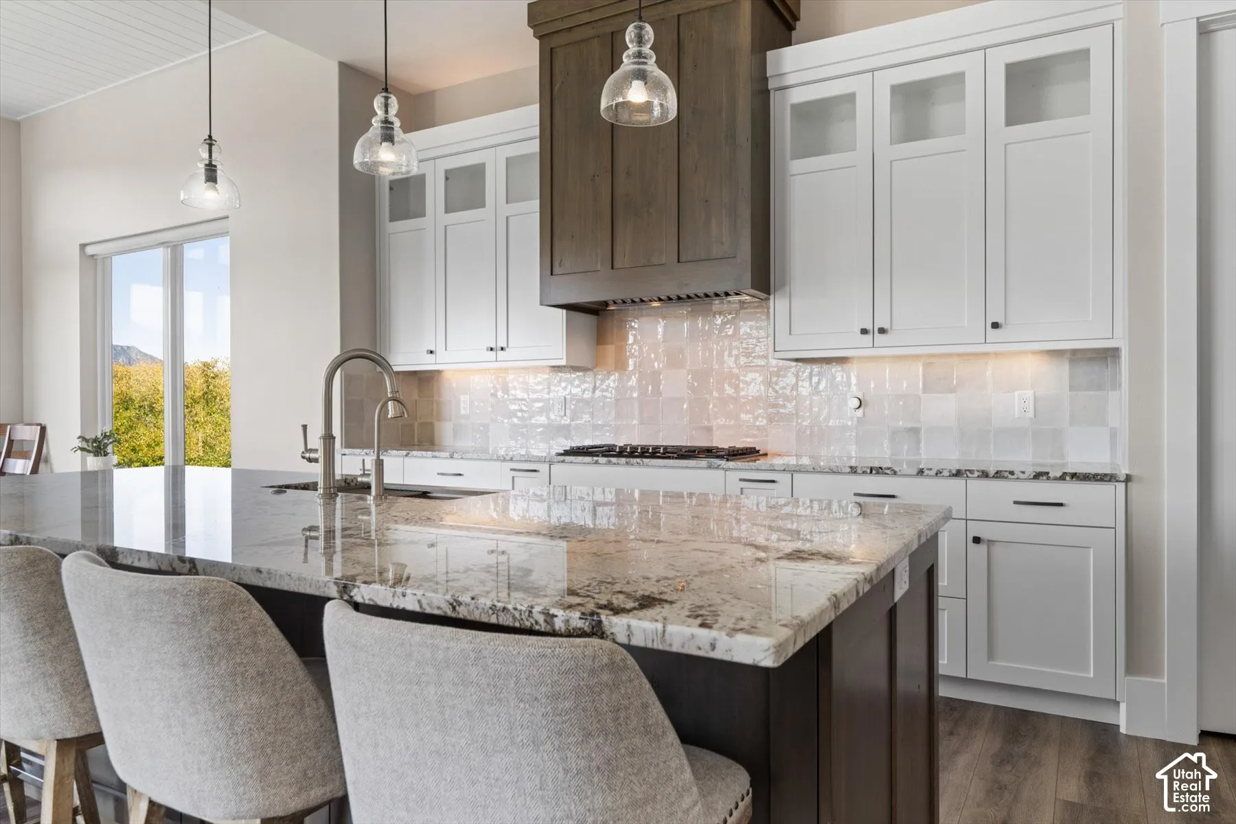 Kitchen featuring a central island with a stone countertop, a stainless steel gooseneck faucet, a white tile backsplash, and white cabinetry