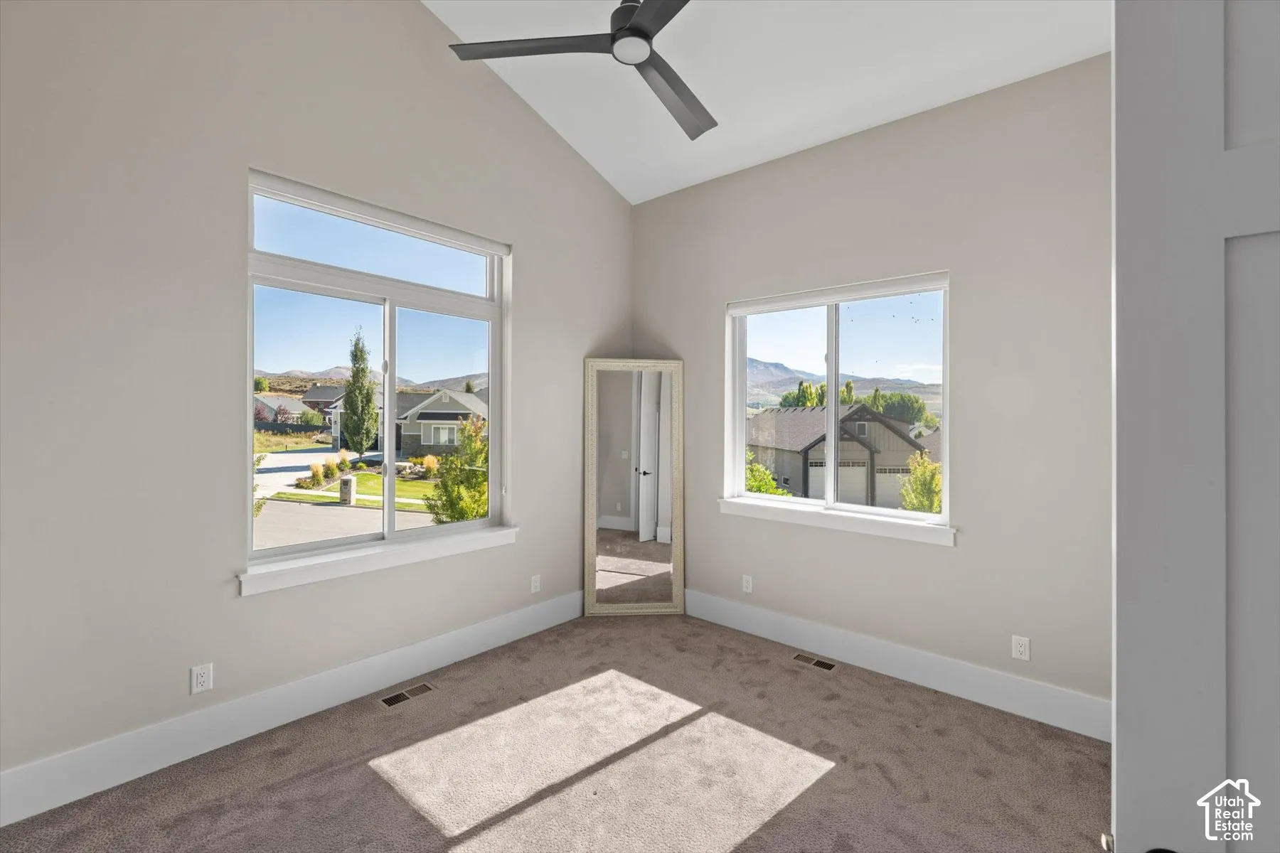 Vaulted ceiling with a ceiling fan, two windows, and neutral carpeting