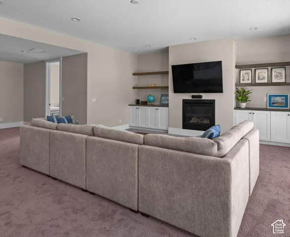 Recessed lighting, built-in cabinetry with floating shelves, and a fireplace with a mounted television
