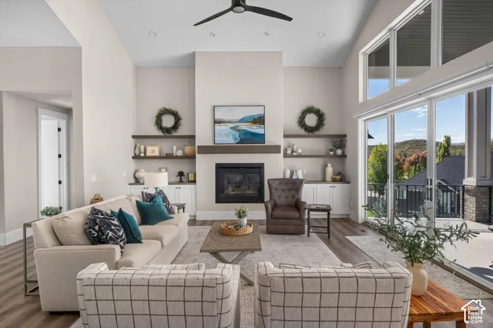 Vaulted ceiling with a ceiling fan, fireplace with a wood-finish mantel, built-in shelving, glass sliding doors, and wood-finish flooring