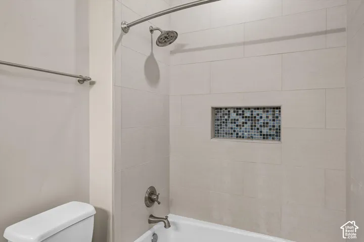 Bathtub with light-toned rectangular tile surround, recessed mosaic tile niche, brushed nickel showerhead, and matching faucet fixtures