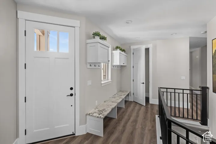 Entryway featuring a paneled door with glass inserts, wood-finish flooring, a built-in bench with a stone-finish top, and built-in wall cabinets with hooks