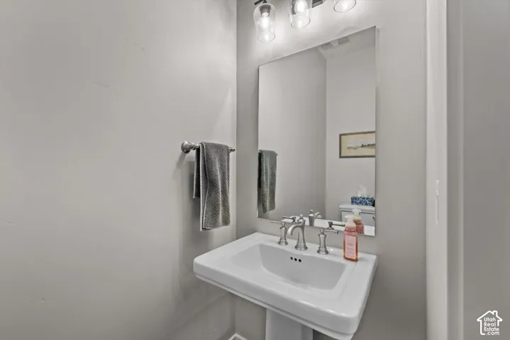 Pedestal sink with brushed nickel faucet, wall-mounted mirror, and overhead vanity lighting