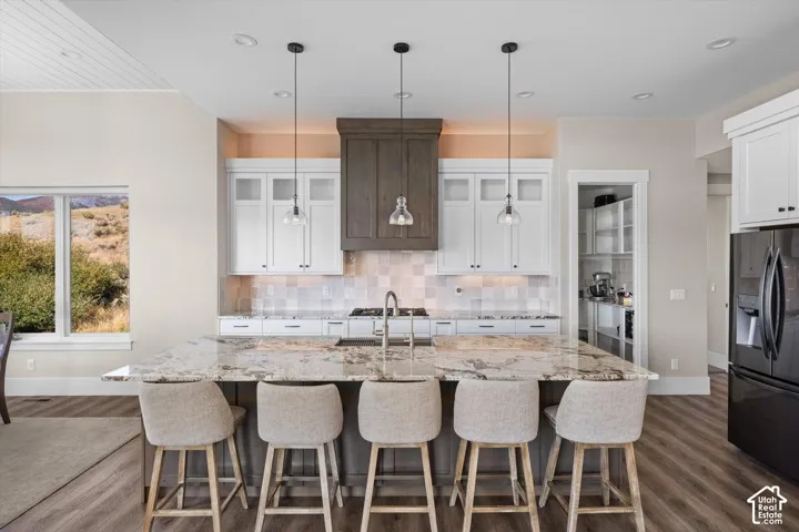 Spacious kitchen island with seating, pendant lighting, white cabinetry, and a full-size refrigerator