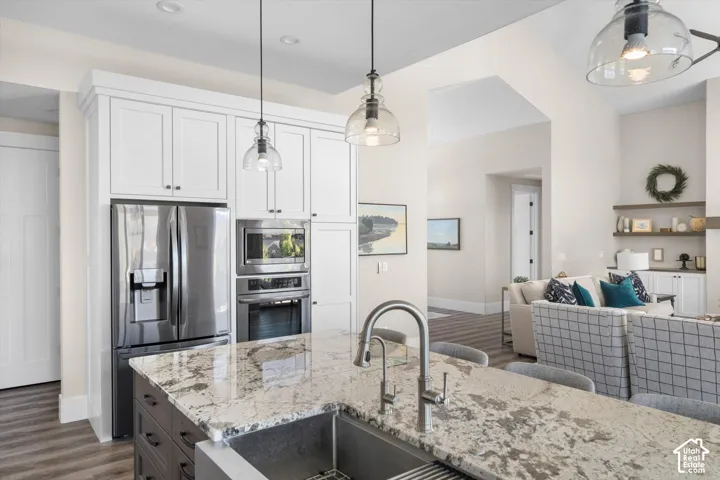 Kitchen island with stone countertop and integrated sink, stainless steel appliances, white upper cabinetry, recessed lighting, and wood-finish flooring