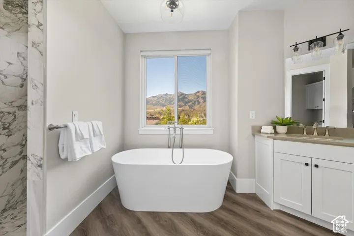 Freestanding soaking tub with a floor-mounted faucet, wood-finish flooring, and a window with mountain scenery