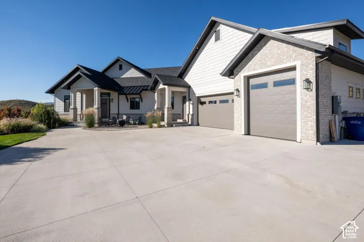 Modern exterior featuring light-colored brick and siding, a multi-car garage with contemporary doors, a concrete driveway, and a covered entry