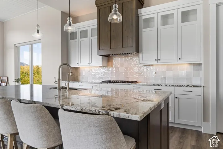 Kitchen featuring a central island with a stone countertop, a stainless steel gooseneck faucet, a white tile backsplash, and white cabinetry