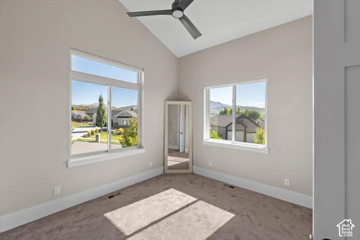 Vaulted ceiling with a ceiling fan, two windows, and neutral carpeting