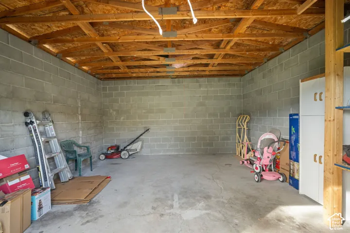 Concrete block walls, exposed wood beam ceiling, concrete flooring, built-in shelving, and storage cabinetry