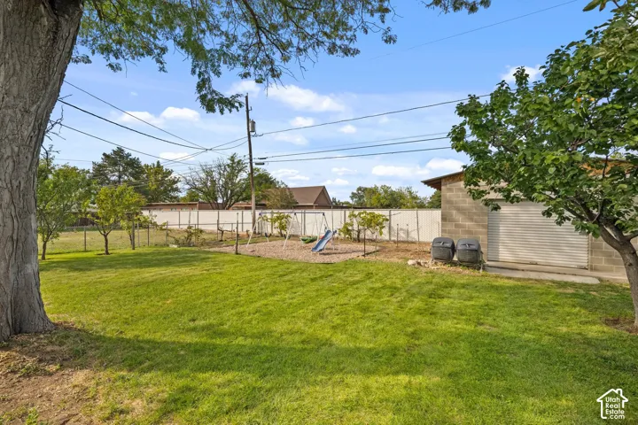 Expansive grassy yard with mature trees and a block-constructed outbuilding featuring a roll-up door