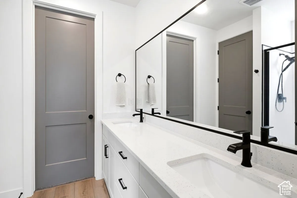 Dual-sink vanity with white cabinetry, light-flecked quartz countertops, matte black fixtures, and a large frameless mirror