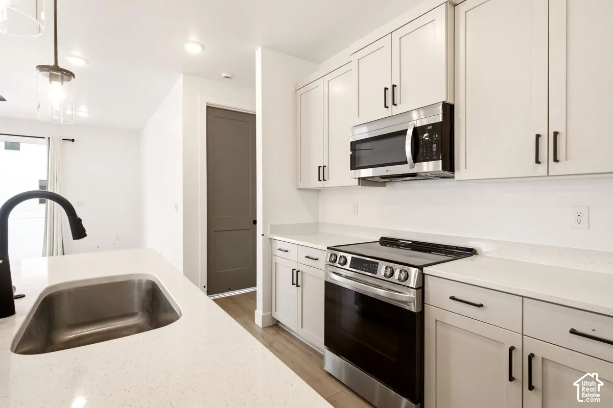 Kitchen featuring Shaker-style cabinetry, quartz countertops, stainless steel appliances, an island with an undermount sink, and matte black hardware