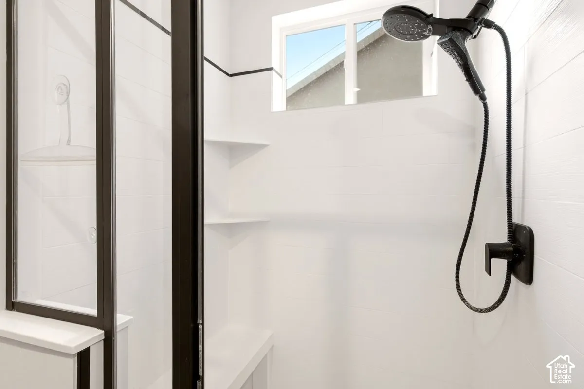 Shower stall featuring white subway-tiled walls, a matte black handheld shower fixture, built-in corner shelving, a recessed shower seat, and a glass door with a dark metal frame