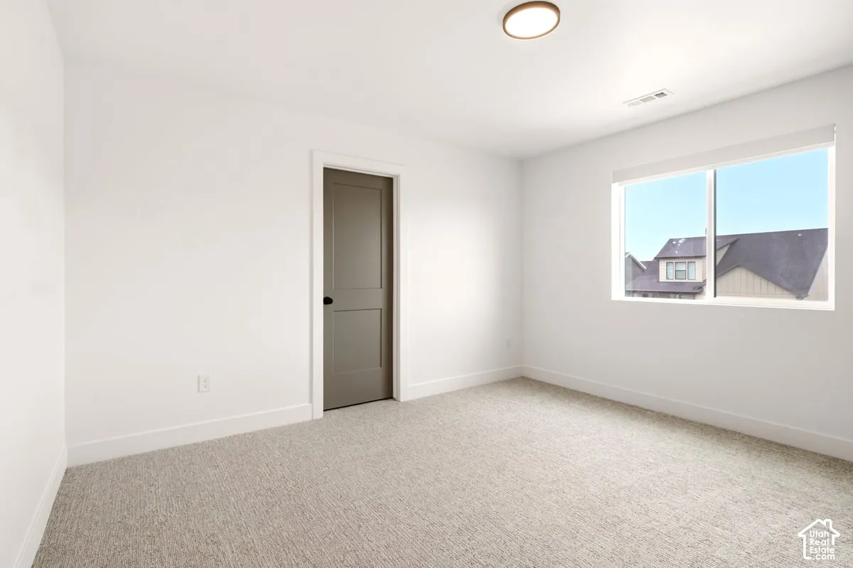 Neutral-toned interior space featuring light-colored wall-to-wall carpeting, white walls, a single-panel interior door with matte black hardware, and a large horizontal window