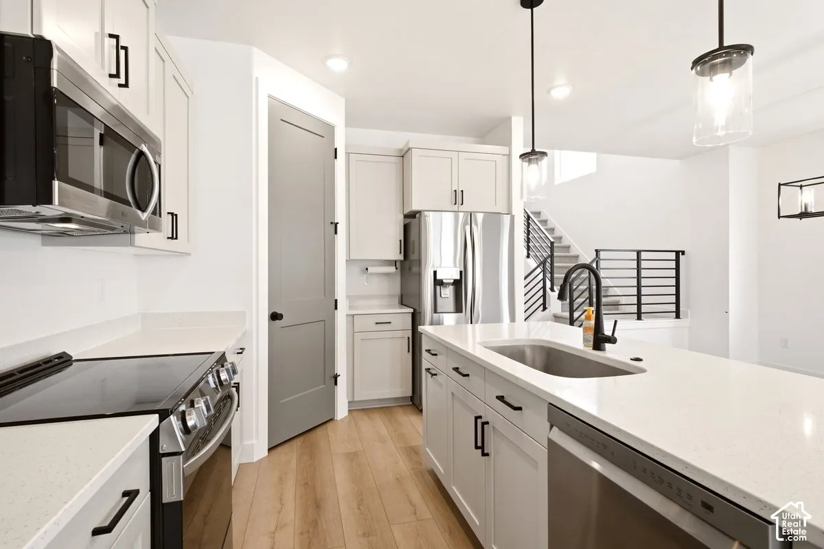 Kitchen featuring white cabinetry, solid surface countertops, stainless steel appliances, wood-finish flooring, and pendant lighting