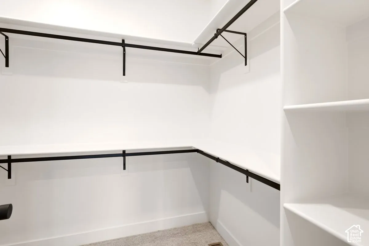 Walk-in storage space featuring tiered white shelving, black metal clothing rods, integrated vertical shelving units, and neutral carpeting