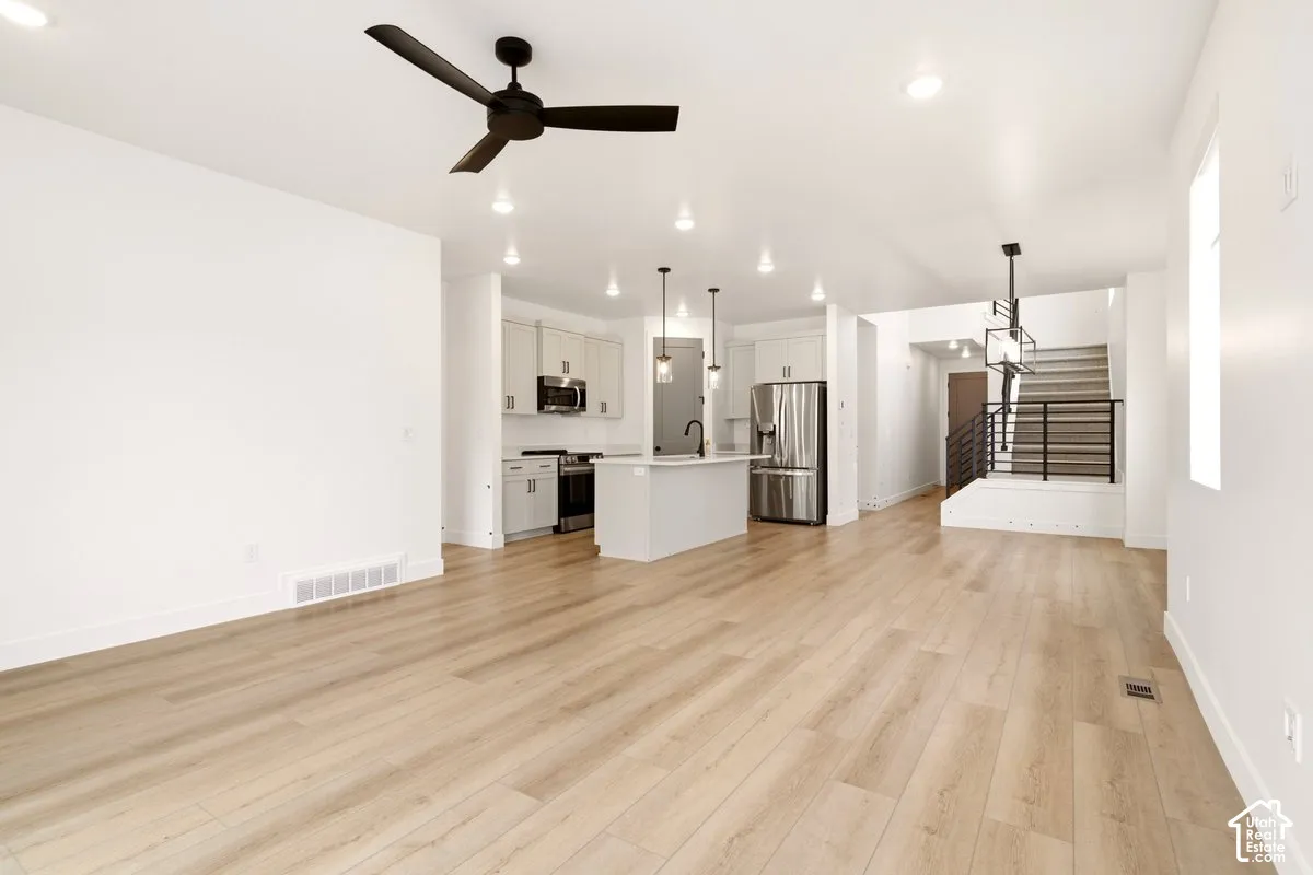 Open-concept floor plan featuring wood-finish flooring, kitchen with center island and stainless steel appliances, matte black light fixtures, and a staircase with metal railing