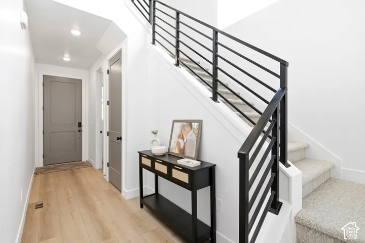 Wood-finish flooring, recessed lighting, solid core doors, and a carpeted staircase with a modern black railing