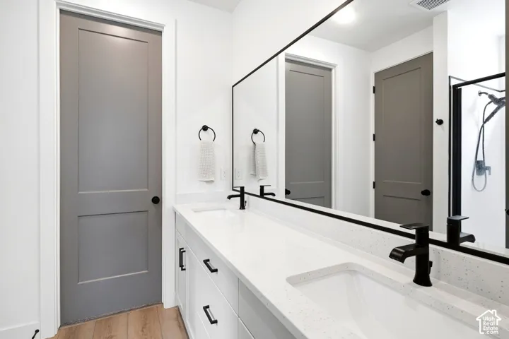 Dual-sink vanity with white cabinetry, light-flecked quartz countertops, matte black fixtures, and a large frameless mirror