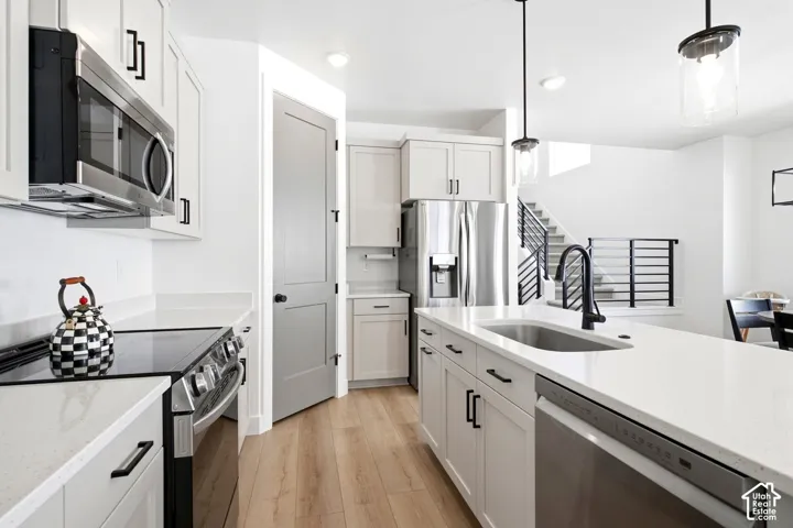 Modern kitchen featuring light wood-finish flooring, white cabinetry, stainless steel appliances, and a central island with a sink and matte black faucet