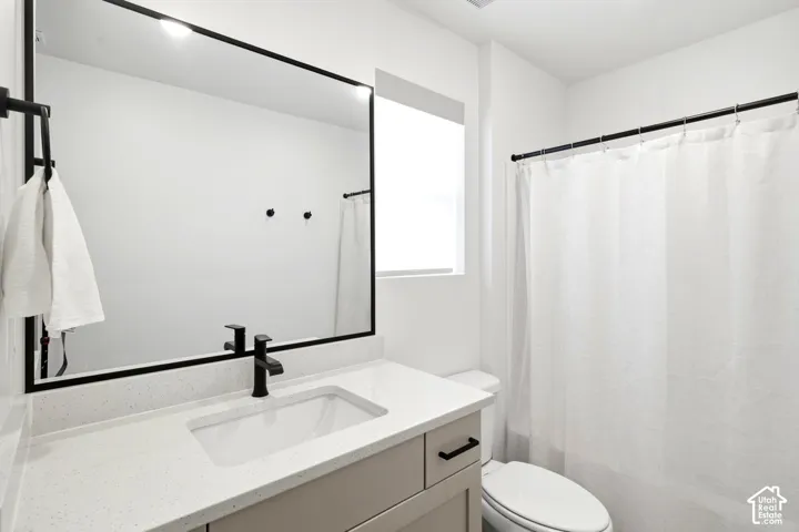 Bathroom vanity with a light-toned cabinet, white solid-surface countertop, rectangular undermount sink, matte black faucet, and large rectangular mirror with a black frame