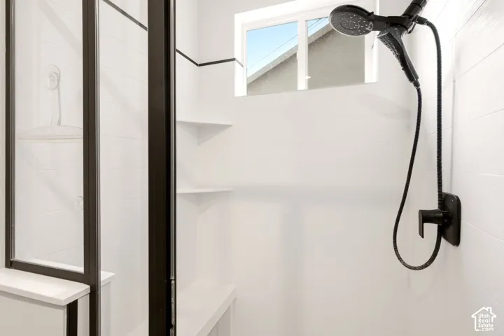 Shower stall featuring white subway-tiled walls, a matte black handheld shower fixture, built-in corner shelving, a recessed shower seat, and a glass door with a dark metal frame