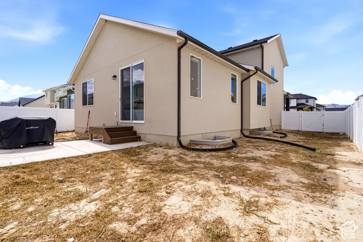 Exterior stucco finish with a white vinyl fence, offering a concrete patio and a sliding glass door