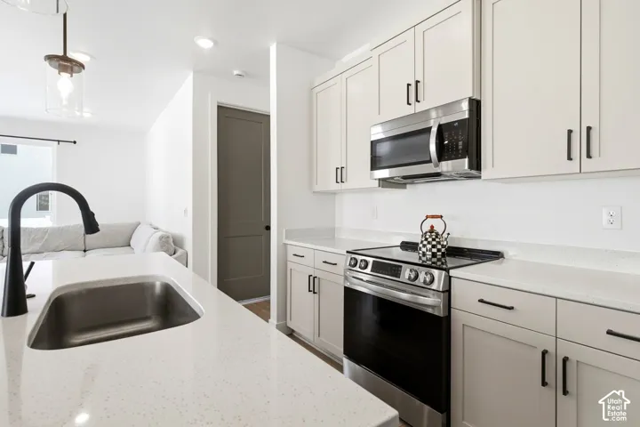 Kitchen featuring a stainless steel sink with a matte black faucet, light-toned countertops, painted cabinetry with dark hardware, stainless steel microwave, and a stainless steel electric range